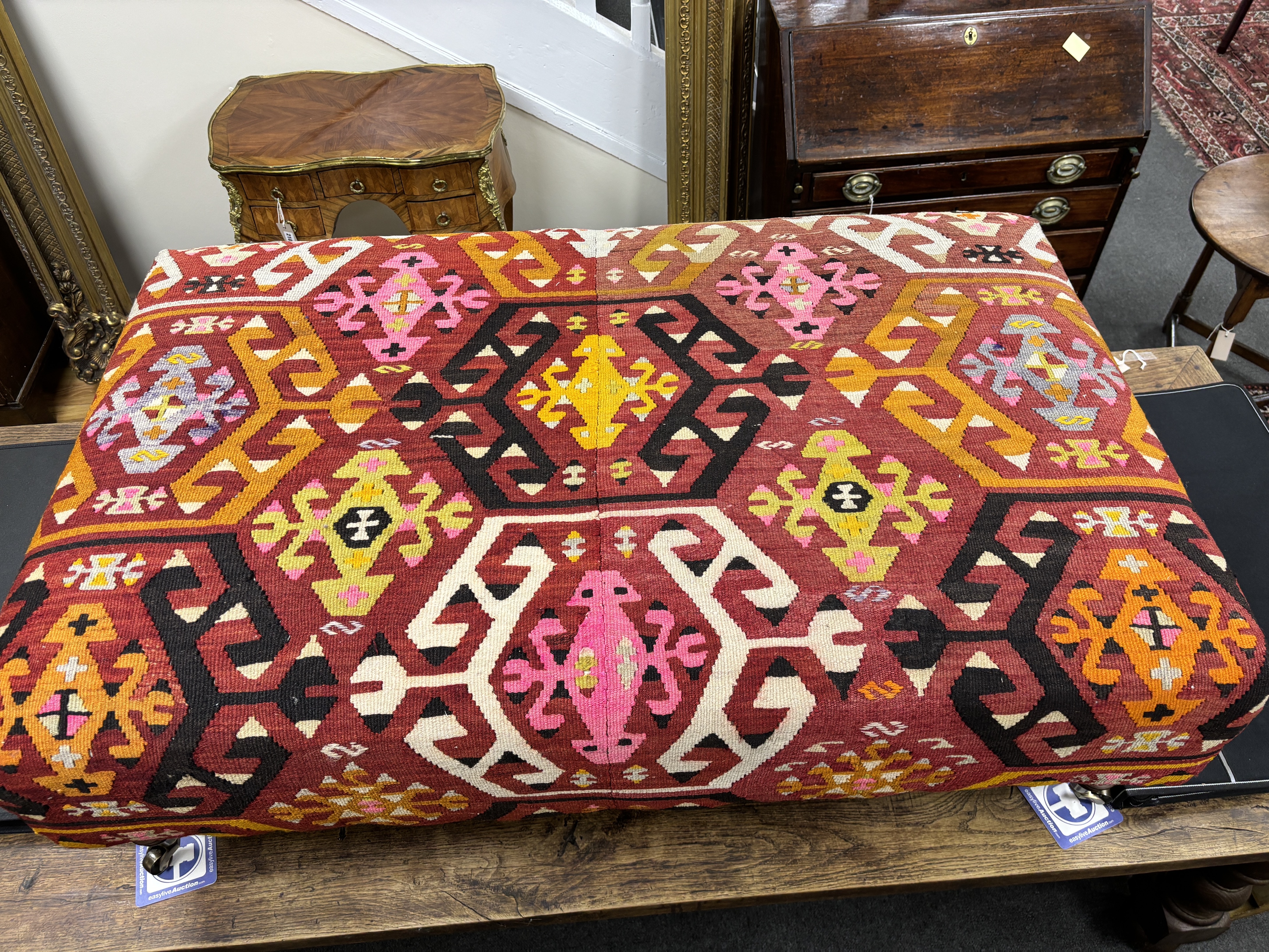 A large contemporary rectangular footstool with antique polychrome Kilim upholstery on turned beech feet with brass caps and castors, width 124cm, depth 78cm, height 40cm.